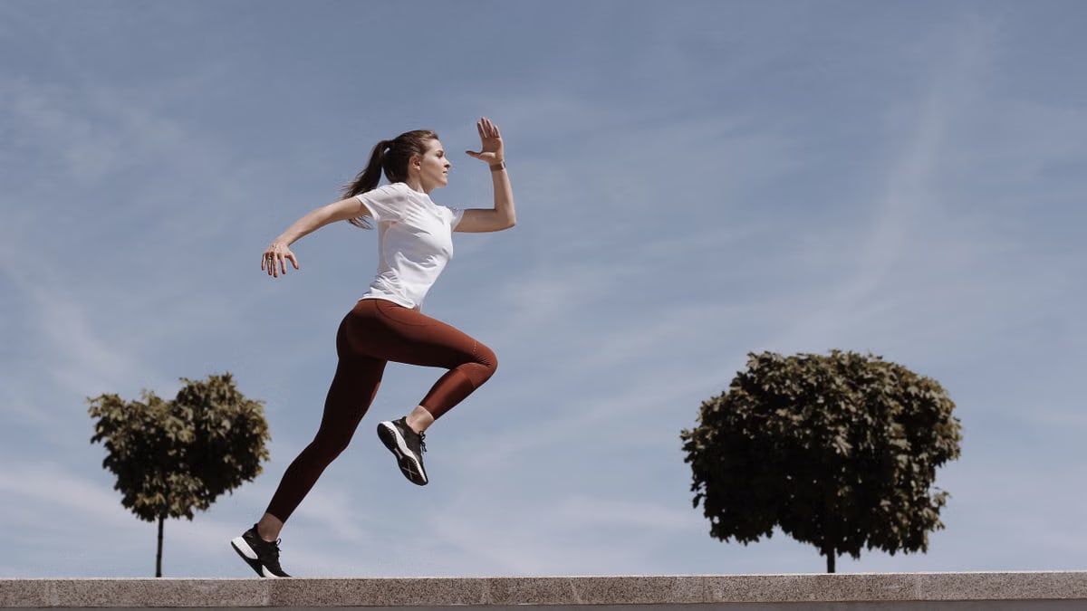 Athletic woman running on an outdoor road, demonstrating fitness and determination under a blue sky.